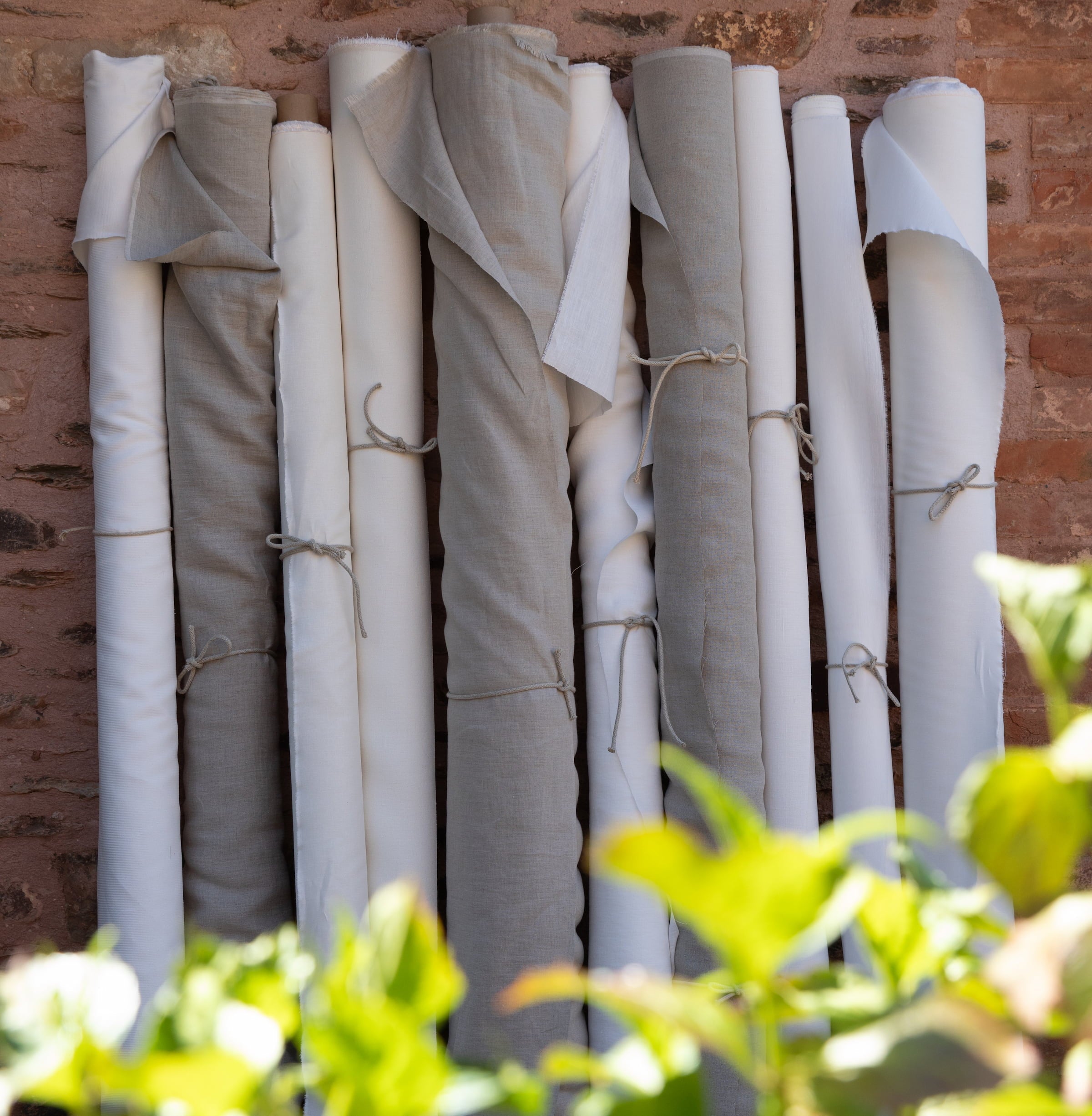 rolls of natural hemp fabrics against a wall with greenery in foreground