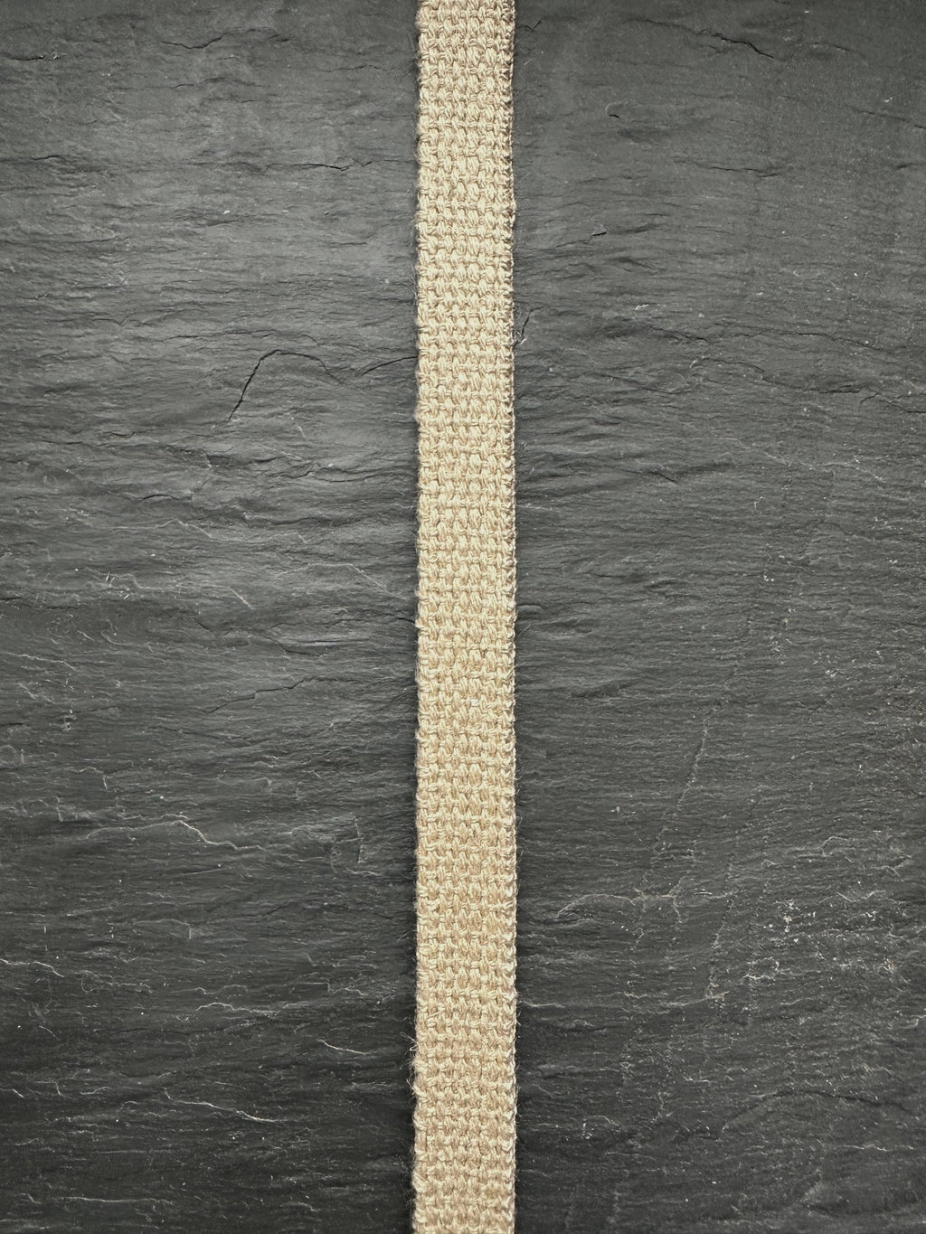 Narrow natural hemp webbing strip on a dark gray textured background
