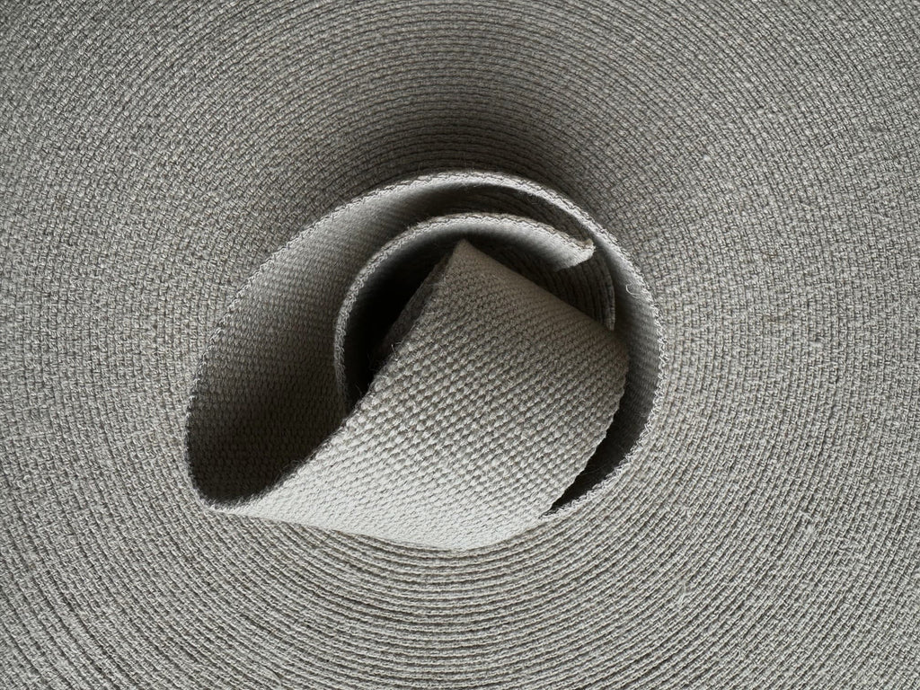 Close-up of a roll of grey natural hemp webbing fabric with a textured surface.
