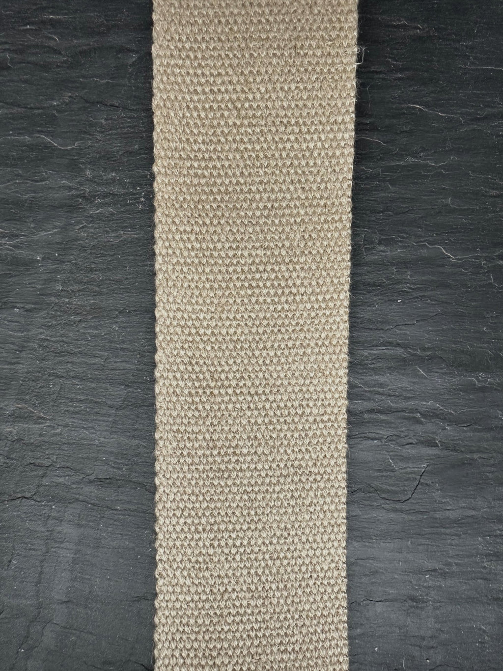 Beige woven natural hemp webbing strip on a dark textured background