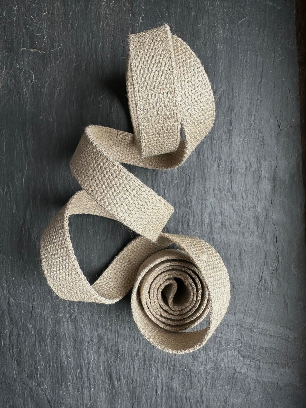 Beige woven hemp webbing piece on a dark textured surface