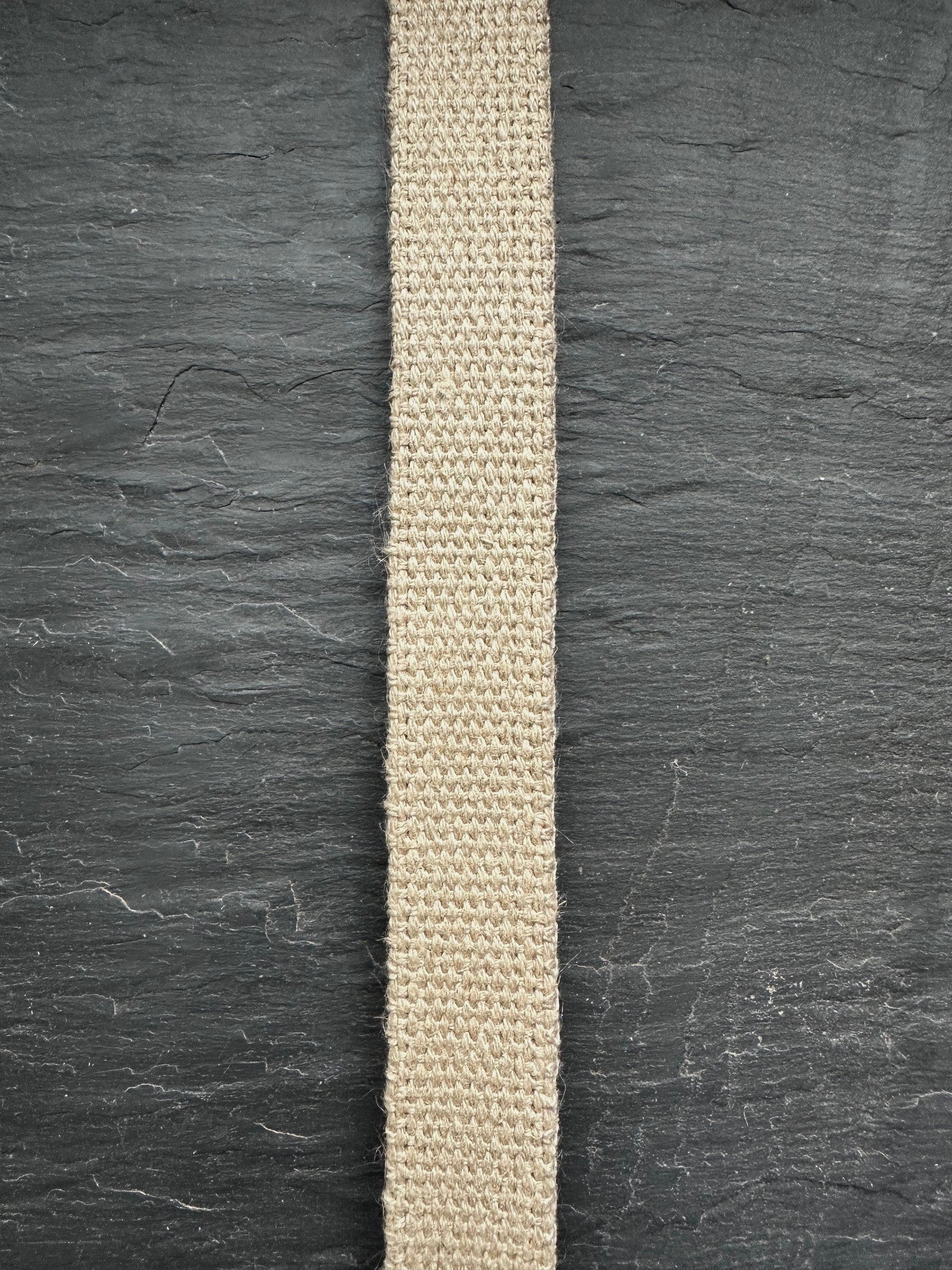 Beige woven hemp webbing strip on a dark slate surface