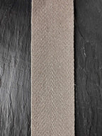 A close-up of a woven herringbone pattern hemp webbing tape  in a light beige or taupe color, positioned horizontally on a dark charcoal textured slate panel.