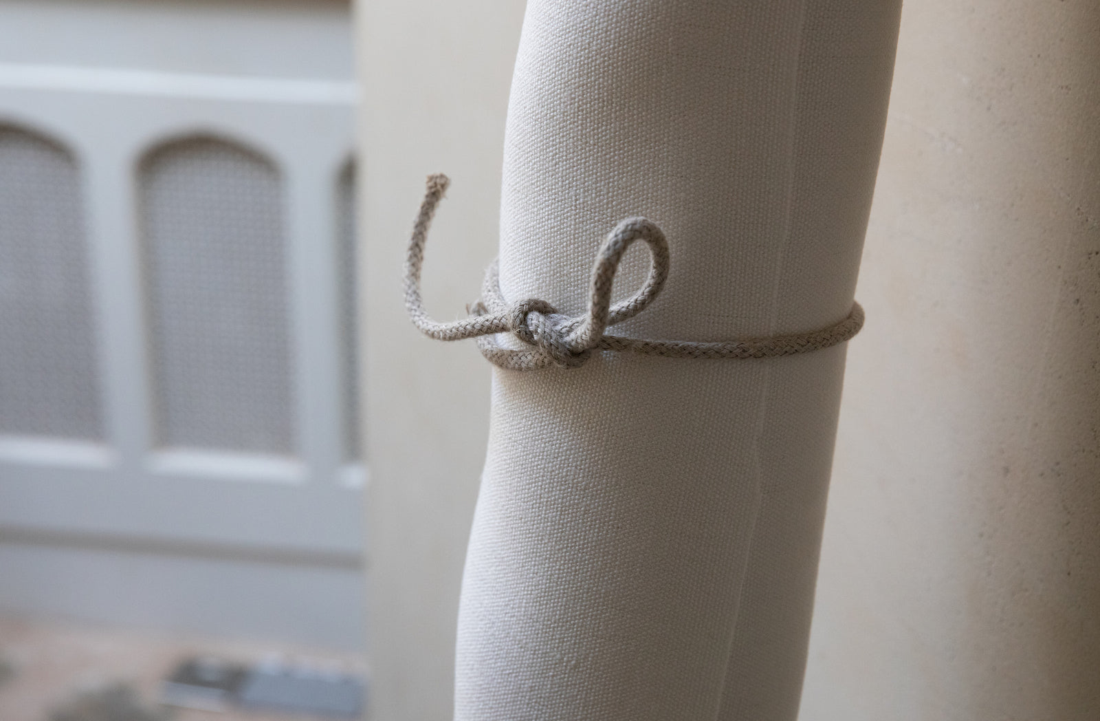 Close-up of an ivory hemp fabric roll with a knotted tieback against a neutral background