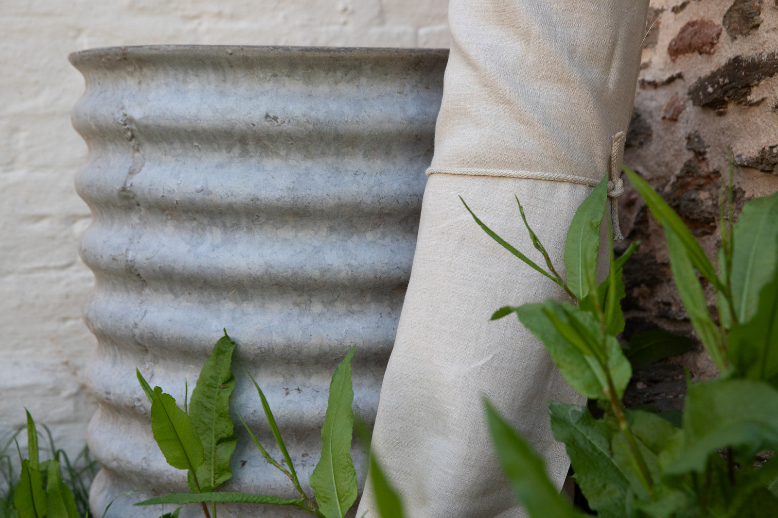 Hemp fabric roll with a metal water tank and green plants in the foreground.