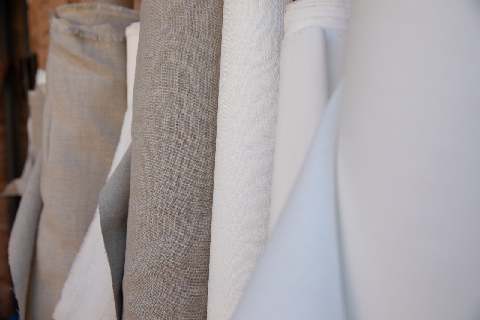 Rolls of hemp fabric in various colors, including beige and white, against a wall