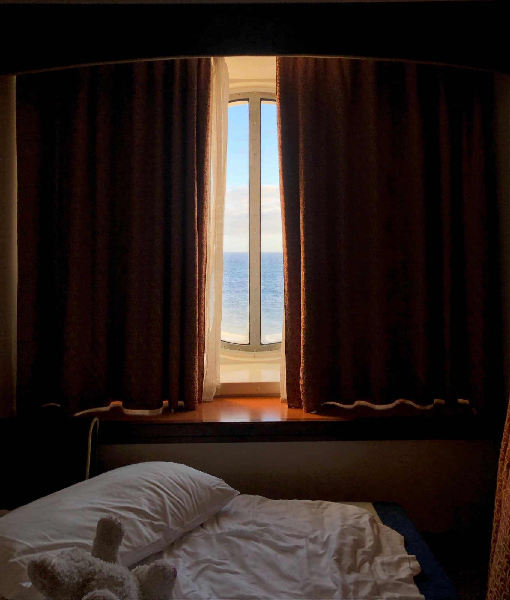 Bedroom with an open window showing a bright outdoor scene, curtains partially drawn.