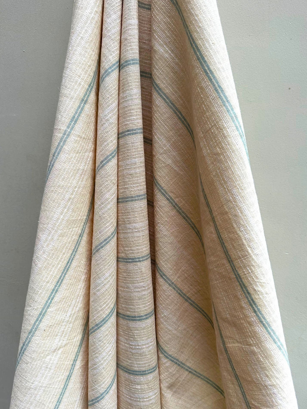 Close-up of Dune hemp fabric with blue stripes hung on a plain background
