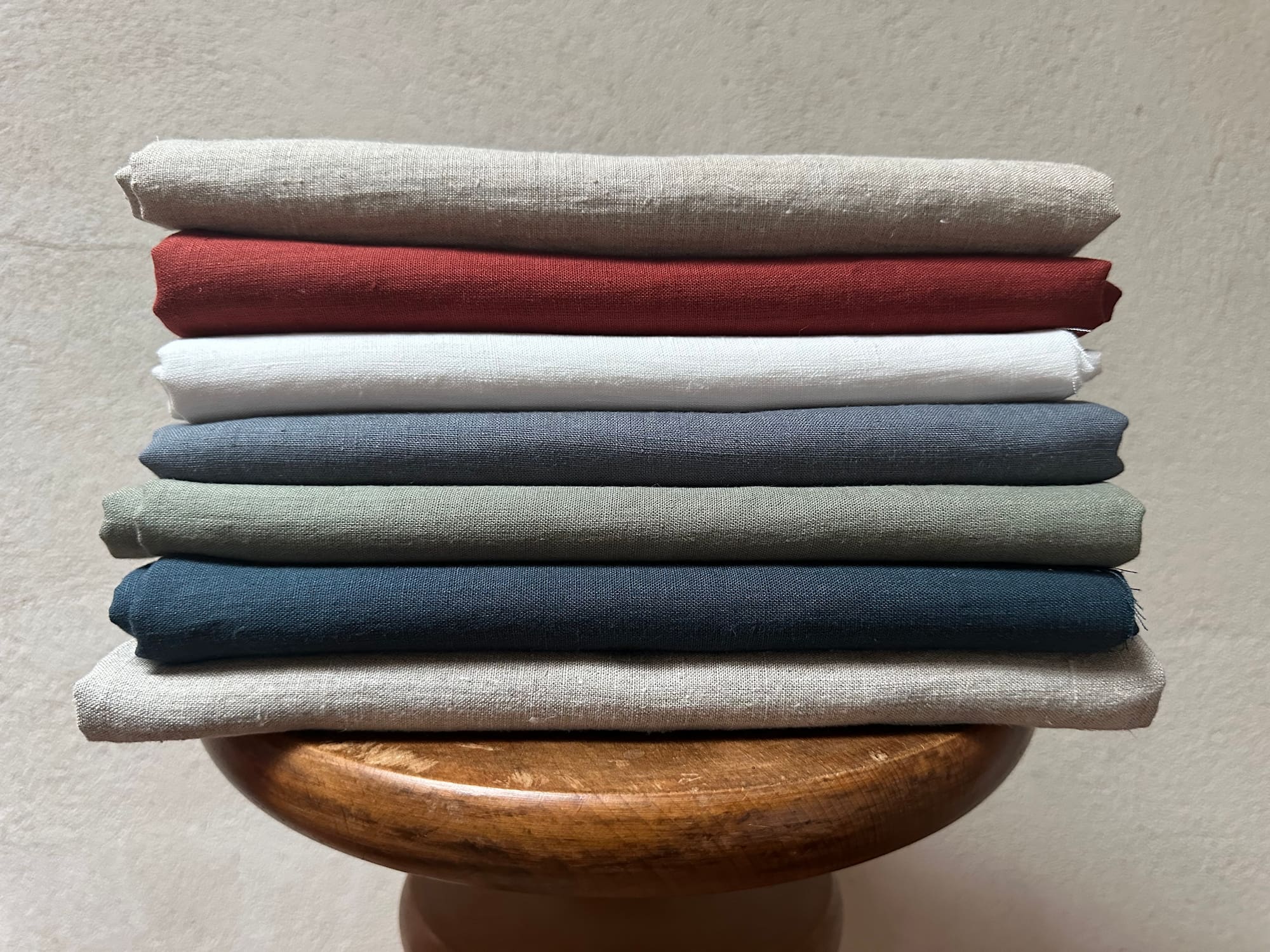 Stack of folded Willow hemp fabric swatches in various colors on a wooden stand against a neutral background